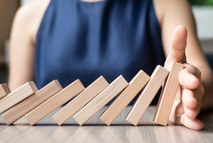 Hand stopping falling dominoes, business risk management concept